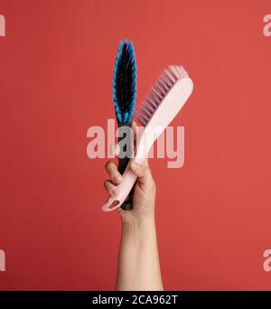 female hand holds black plastic cleaning brush, red background, close up Stock Photo