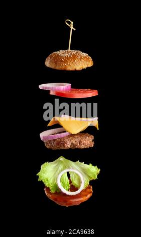 Flying ingredients of a classic cheeseburger: sesame bun, onion rings, tomato slices and a juicy barbecue cutlet on a black background. Fast food Stock Photo