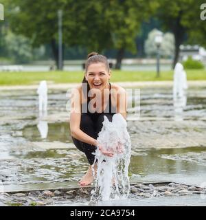 Attractive girl happily plays with fountain water stabs in city park. Stock Photo