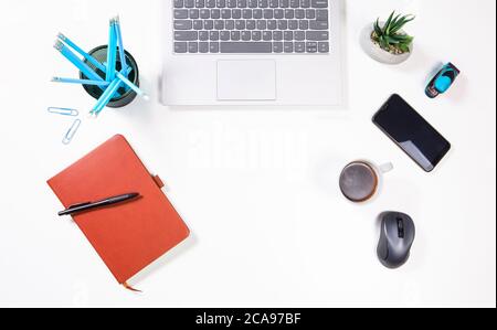 Office workplace table top view with coffe, smartphone, laptop and notepad. Workplace view from above on white desk. Copy space on white background. Stock Photo