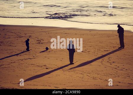 Silhouette of a family playing football in the sunset on the beach in Morocco Stock Photo