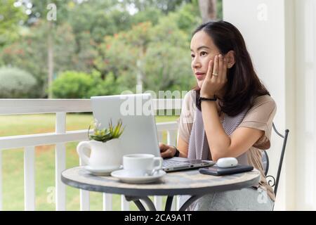 Thoughtful businesswoman work on laptop hands on her chin looking in distance. Stock Photo