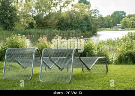 Tranquil scene with two deck chairs chairs on a green lawn in a park and a lake landscape in the background Stock Photo