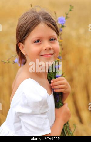 Little girl with a bouquet of wildflowers in her hands in a wheat field.