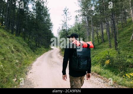 Young male nature explorer walking on the dirt road through the forest Stock Photo