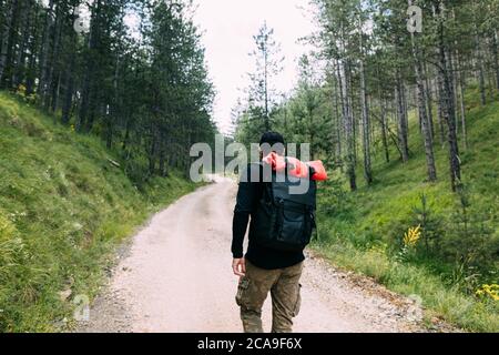 Young male nature explorer walking on the dirt road through the forest Stock Photo
