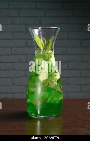 Green cocktail tarragon in a glass decanter on a wooden table against a brick wall. Photos for restaurant, cafe and bar menus Stock Photo