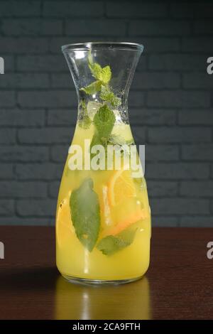 Cold lemon yellow cocktail lemonade in a glass decanter on a wooden table against a brick wall. Photos for restaurant, cafe and bar menus Stock Photo