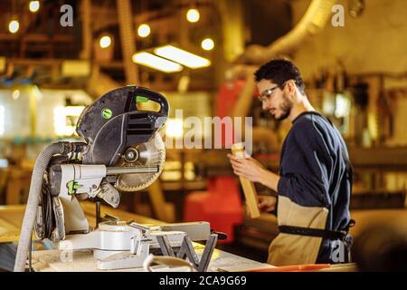 caucasian carpenter preparing wooden furniture for customers, work on an order, use electric machine for sawing and cutting, handicraft, carpentry con Stock Photo