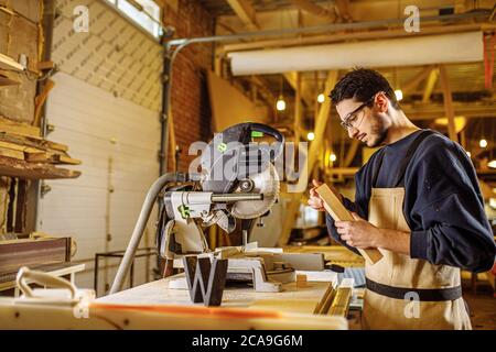 portrait of concentrated carpenter man at work place, skillful guy in uniform make furniture on an order for cutomers Stock Photo