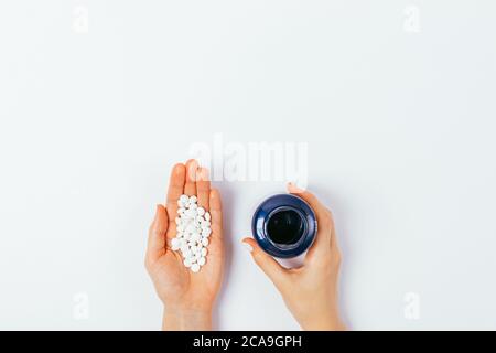Woman's palm with handful of pills and hand holding jar container on white table, top view. Stock Photo