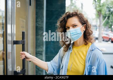 Young woman in protective mask opens the door Stock Photo
