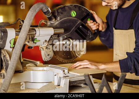 young caucasian hard working carpenter using circular saw, craftsman hold powerful electric machine for wood cutting