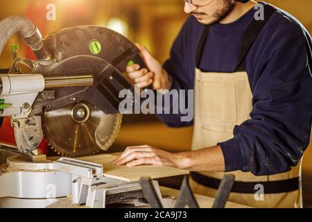 caucasian carpenter preparing wooden furniture for customers, work on an order, use electric machine for sawing and cutting, handicraft, carpentry con Stock Photo
