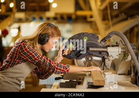 caucasian woman carpenter drives a circular saw, concentrated woman work in factory contrary to opinion that this is a man s job. feminism concept Stock Photo