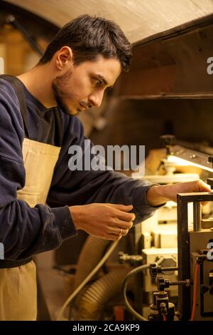 portrait of concentrated carpenter man at work place, skillful guy in uniform make furniture on an order for cutomers Stock Photo