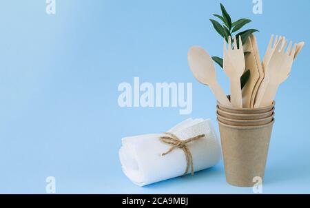 Eco natural wooden cutlery (knives, spoons, forks) in craft paper cup next to paper napkins on blue background. Eco sustainable living Stock Photo
