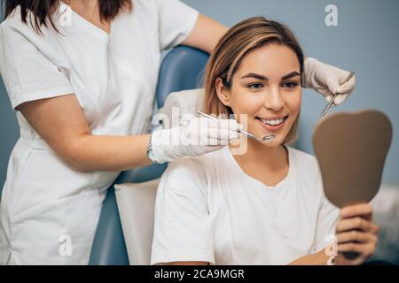 young and beautiful woman look at mirror after teeth treatment by professional dentist. Medicine concept Stock Photo