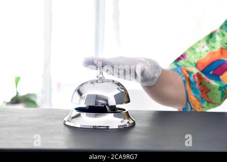 Hand of a man wearing colorful shirt and protective gloves rings hotel bell Stock Photo