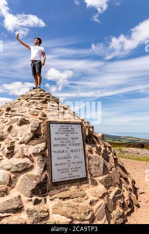 Exmoor National Park - A young man taking a selfie on top of the cairn marking the highest point on Exmoor, Dunkery Beacon, Somerset UK Stock Photo