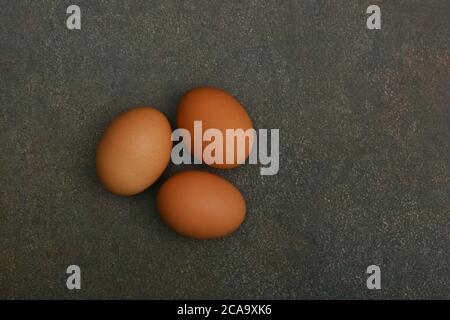 Close up three brown chicken eggs on dark grunge table surface, elevated top view, directly above Stock Photo