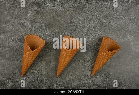 Close up three empty wafer ice cream cones on gray table, elevated top view, directly above Stock Photo
