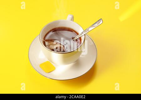 Morning sun shines on yellow table with white porcelain cup full of hot tea, bag still in Stock Photo