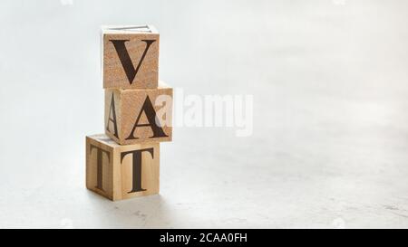 Pile with three wooden cubes - letters VAT meaning Value Added Tax on them, space for more text / images at right side. Stock Photo