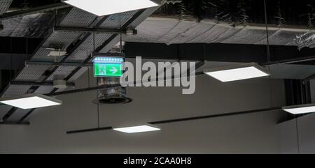 Illuminated green emergency / fire exit sign with running man pictogram on industrial roof. Stock Photo