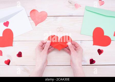 Female hands hold a broken heart with wedding rings on a wooden table. Marriage problems, divorce Stock Photo