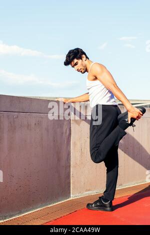 vertical photo of a handsome sportsman stretching his leg muscles on a concrete wall, concept of urban sport and healthy lifestyle, copy space for tex Stock Photo