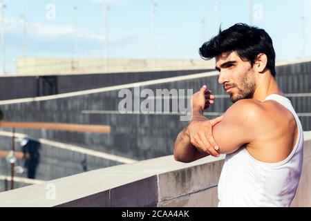 handsome sportsman stretching his shoulder and back muscles, concept of urban sport and healthy lifestyle, copy space for text Stock Photo