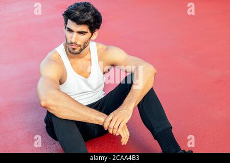 handsome sportsman rest sitting on a red floor, concept of urban sport and healthy lifestyle, copy space for text Stock Photo