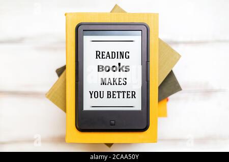 Reading and knowledge. E-book reader is on top of a stack of books on a wooden background. Flat lay. Concept of education and electronic gadgets. Stock Photo