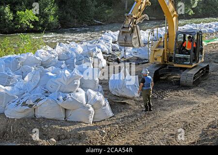 A flood mitigation construction crew using an excavator to lift heavy bags of rocks to stabilize the river banks of the Elbow River, Calgary Canada Stock Photo