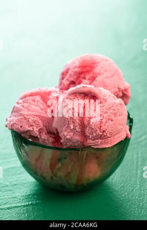 Strawberry ice cream bowl with a red topping, backlit, isolated on a green background. Delicious homemade berries ice cream close-up. Summer dessert. Stock Photo