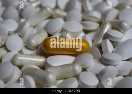 Full frame closeup of pile countless white pills and capsules with one yellow capsule in center (focus on yellow pill) Stock Photo
