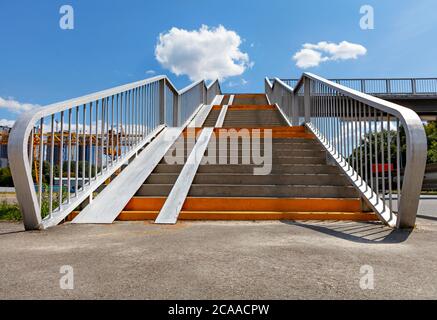 Wide entrance angle of a pedestrian crossing staircase over a highway against a background of blue sky and white clouds, low angle view, copy space. Stock Photo