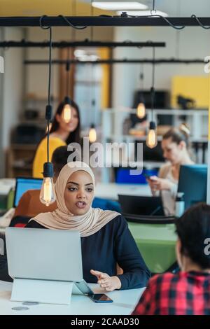 African muslim girl wearing hijab working on a laptop in a modern startup company. Stock Photo