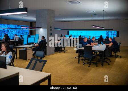 Group of Security data center operators (administrators) working in a group at a CCTV monitoring room while looking at multiple monitors ( computer sc Stock Photo