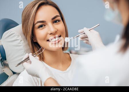 portrait of young caucasian woman with perfect smile in dental office, come to treat spoiled teeth, look at camera Stock Photo