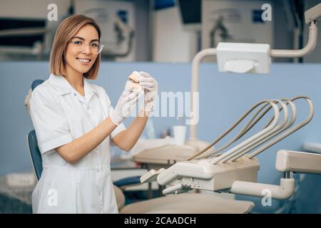 portrait of beautiful dentist woman holding prosthesis in hands, wearing white doctor's uniform, professinal specialist orthodontist Stock Photo