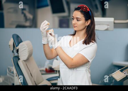 portrait of beautiful dentist woman holding prosthesis in hands, wearing white doctor's uniform, professinal specialist orthodontist with prosthesis Stock Photo