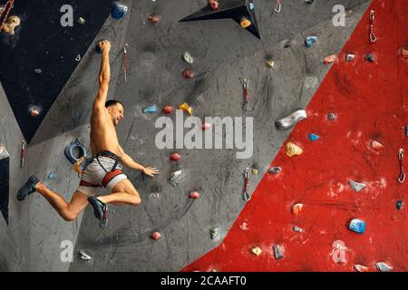 Male climber instructor practicing rock climbing on artificial wall painted in red and grey coloures indoors. Active lifestyle and bouldering concept. Stock Photo