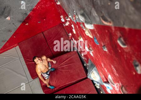 Top view of shortless athletic man bouldering at indoor climbing centre. climber practicing rock climbing at an indoor climbing gym. Stock Photo