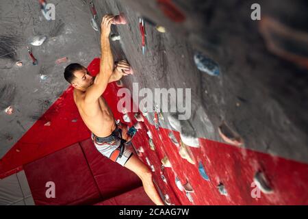 High angle view of sportsman bouldering at an indoor climbing centre. Determined climber practicing rock climbing at an indoor climbing gym. Stock Photo