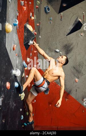 Distant shot of female climber exercising in gym. Focus on artificial grey wall with boulders. Stock Photo