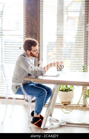 Concentrated husband in casual wear checking bank reporting, sitting at the table in the living room at home. Stock Photo