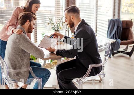Caucasian respectable couple buying apartment, buyers of real estate ready to conclude a deal with real estate agent after signing documents for realt Stock Photo
