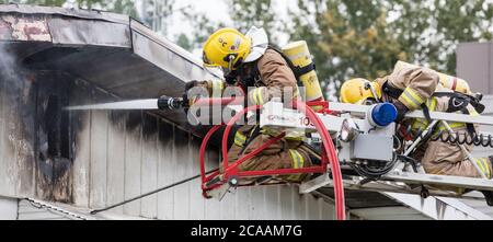 Firefighters spray water on roof with hose from ladder. Stock Photo